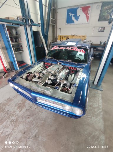 Blauer Sportwagen mit offenem Motorraum in einer Werkstatt.